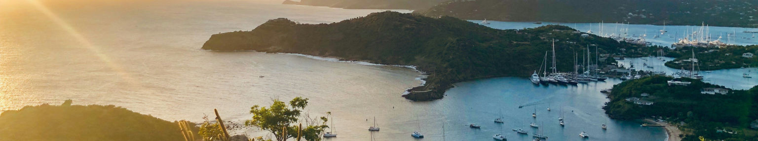Crewed sailing yacht with captain at the helm passing The Baths at Virgin Gorda in the BVI, the chef preparing lunch on the aft deck, Borrow A Boat Caribbean captained yacht charter